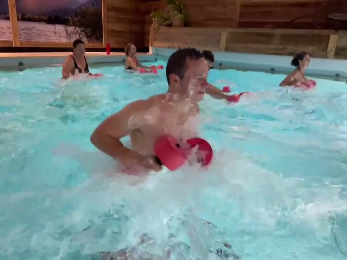 Teilnehmer mit Aqua-Hanteln im Vordergrund einer Trainingsgruppe im Pool