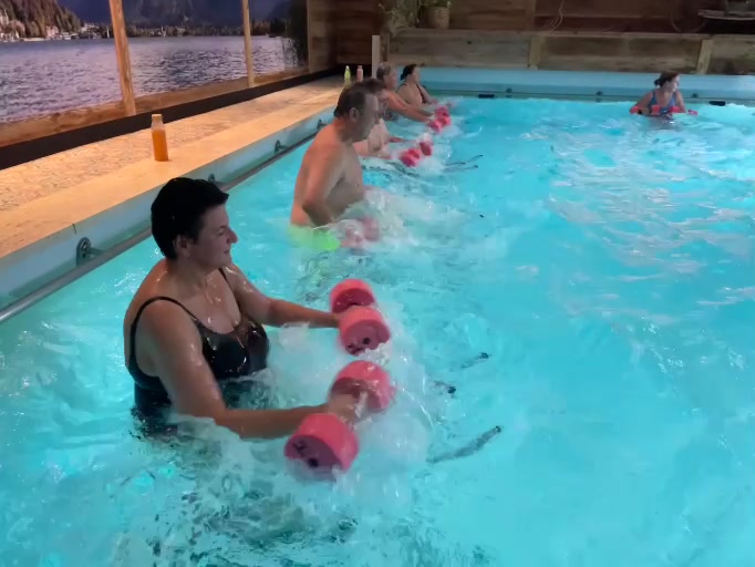 Teilnehmende bewegen Aqua-Hanteln vor dem Körper im Wasser